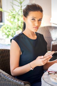 Portrait of beautiful young caucasian businesswoman with cell phone sitting in the cafe