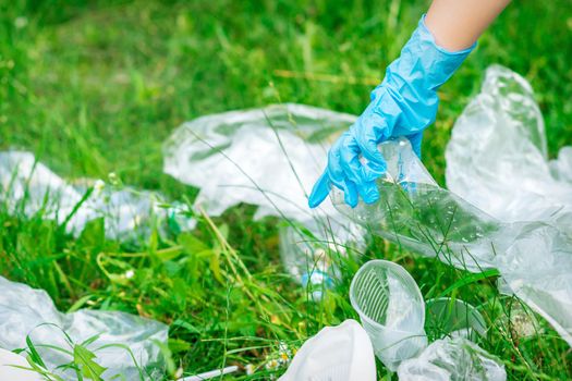 Hand of child cleans the park from plastic debris lying on the green grass