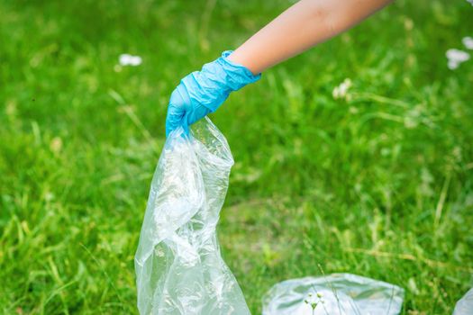 Hand of child cleans the park from plastic debris lying on the green grass