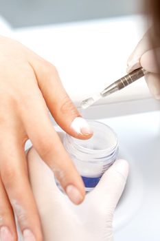 Close up of the process of applying acrylic powder on the nails of a young woman in a beauty salon