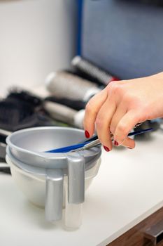 Hand of hairstylist prepares dye in bowl for coloring hair in hairdress salon