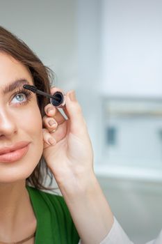 Professional makeup artist applying mascara on lashes of beautiful young caucasian woman in beauty salon