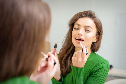 Beautiful young caucasian woman applying gloss to the lips looking in the mirror