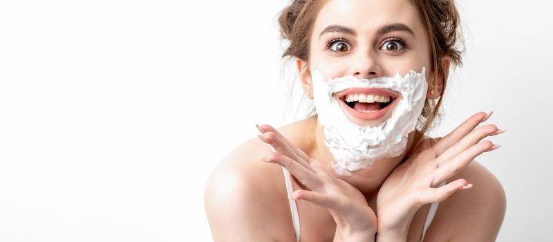 Beautiful young caucasian woman with shaving foam on her face posing on white background
