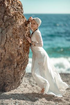 Middle aged woman looks good with blond hair, boho style in white long dress on the beach decorations on her neck and arms