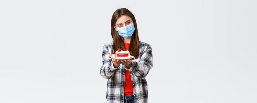 Coronavirus outbreak, lifestyle during social distancing and holidays celebration concept. Tender caring girlfriend made homemade cake, giving it to you, wear medical mask and smiling.