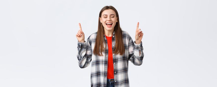 Lifestyle, different emotions, leisure activities concept. Dreamy and happy pretty young woman in checked shirt, dream came true, showing summer vacation resort, pointing fingers up with closed eyes.