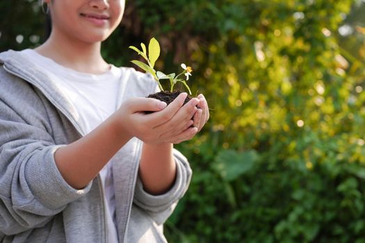 Happy girl with plant in her hand with blurred green nature background. Earth day, environmental concept.