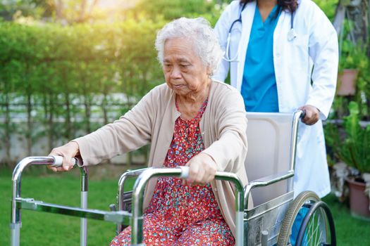 Doctor help Asian elderly woman disability patient walk with walker in park, medical concept.