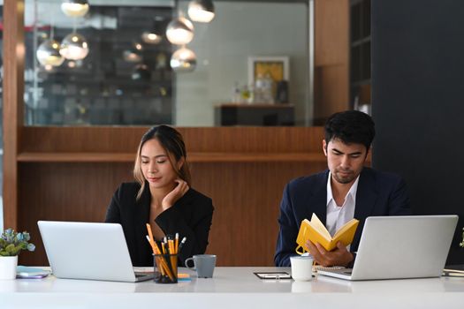 Focused young businesspeople sitting together at office table and working with laptop computer.