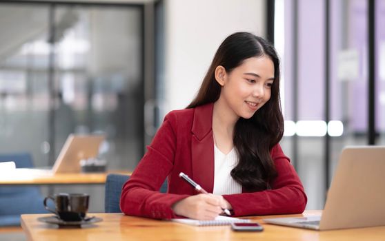 Beautiful Asian businesswoman analyzes charts using laptop calculator at the office..