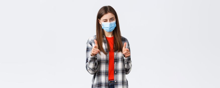 Coronavirus outbreak, leisure on quarantine, social distancing and emotions concept. You can dot it. Supportive young attractive female in medical mask pointing at camera, wink and congratulate.