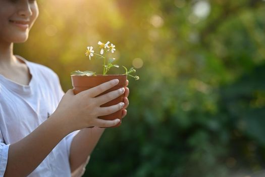 Smiling little girl holding potted plant in hands against blurred green nature background. Earth day, Ecology concept.