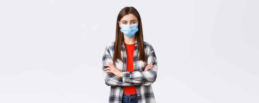 Coronavirus outbreak, leisure on quarantine, social distancing and emotions concept. Confident young woman in checked shirt wear medical mask, cross arms chest, determined look camera.