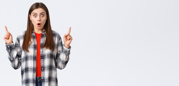 Lifestyle, different emotions, leisure activities concept. Astonished and speechless attractive girl in checked shirt pointing fingers up to tell news, drop jaw staring, make wow expression.