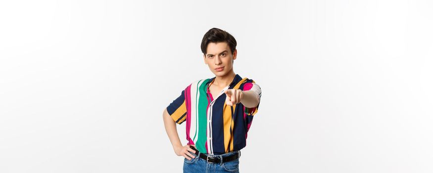 Sassy gay man pointing finger at camera, need you, picking or choosing, standing over white background.