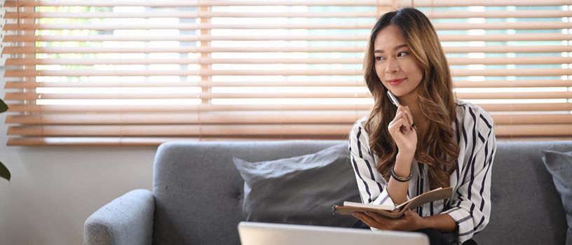 Attractive millennial woman reading book while relaxing on couch at home.