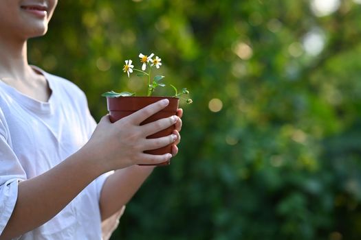 Happy asian girl holding a flower pot in hands. Saving the world, earth day concept.