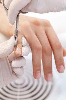 Close up of manicurist using manicure scissors to remove cuticle of female nails in manicure salon
