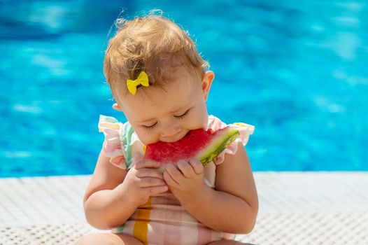 Baby is eating a watermelon by the pool. Selective focus. Kids.