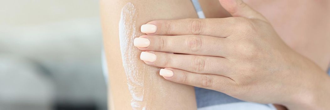 Close-up of young woman applying gently moisturizing body lotion on arm. Take care of her skin condition after shower or bath. Wellness, beauty concept