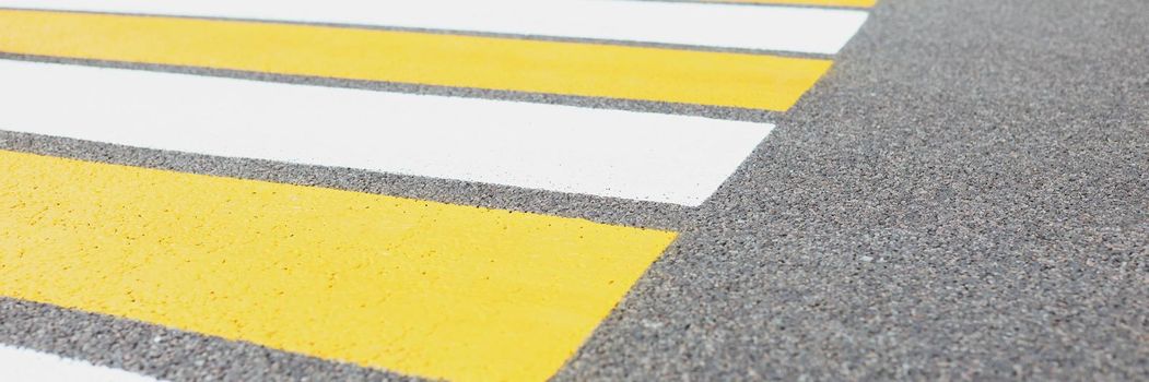 Close-up of marked white and yellow walkway across road or street. Crosswalk or pedestrian crossing. Simply painted lines on asphalt for crossing street safety