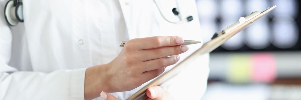 Close-up of doctor in medical gown hold clipboard with prescription paper. Qualified worker examine patients history. Medicine, clinic, healthcare concept