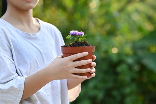 Little girl holding potted plant in hands against blurred green nature background. Saving the world, Ecology, Earth day concept.