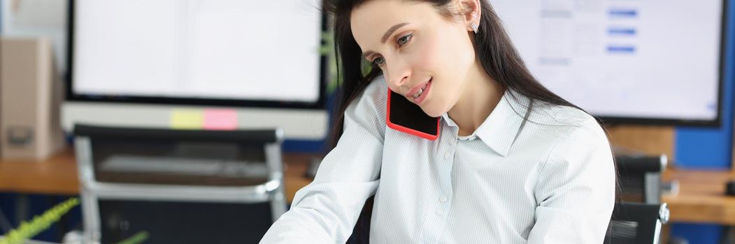 Portrait of woman worker talking on phone and making notes on paper in personal office. Clerk work on digital laptop. Business, career, development concept