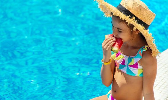 The child eats a watermelon near the pool. Selective focus. Kid.