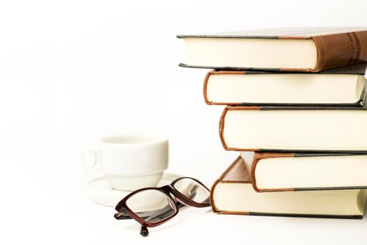 Stacked books next to cup of coffee and eyeglasses on white background