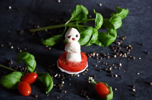 creative snowman canapes of mozzarella and tomatoes on a background of red poinsettia and a scattering of black pepper and green basil. High quality photo