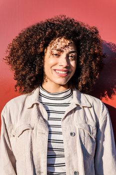 vertical portrait of a beautiful smiling latina woman with curly afro hair on a red background, concept of beauty and diversity