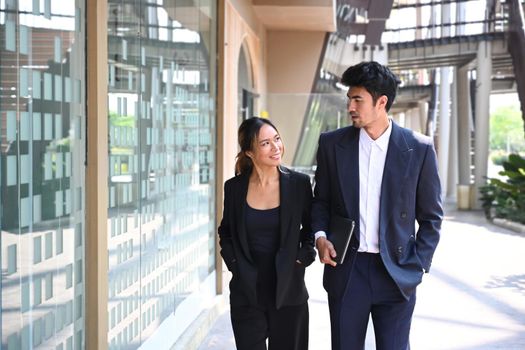 Two executive business people discussion while walking outside modern office building.