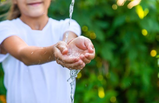 The water flows into the hands of the child. Selective focus. Nature.