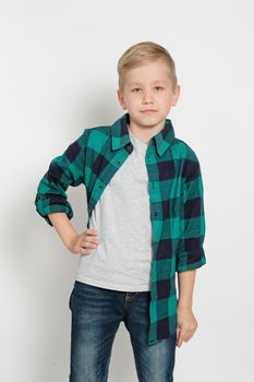 Portrait of cute stylish blond boy kid 7 years old in checked shirt and jeans white background