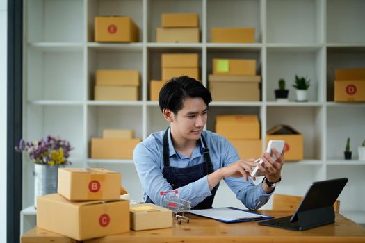 Startup small business SME, Entrepreneur owner using laptop computer taking receive and checking online purchase shopping order to preparing pack product box. Selling online ideas concept.