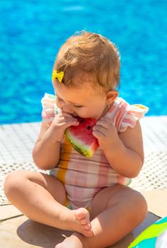 Baby is eating a watermelon by the pool. Selective focus. Kids.