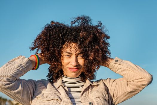 portrait of a beautiful young black woman with a rainbow bracelet smiling and playing with her curly afro hair, concept of beauty, youth and diversity, copy space for text