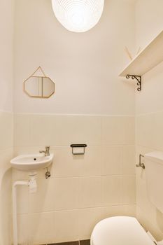 Modern flush toilet and ceramic sink installed on white tiled walls near mirror and towel in small restroom at home