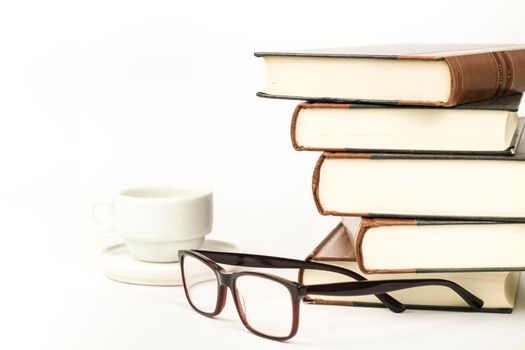 Stacked books next to cup of coffee and eyeglasses on white background