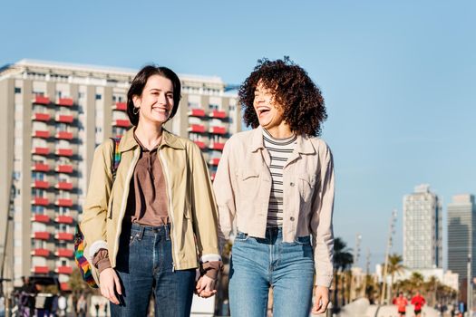 young interracial couple of women walking and laughing around town holding hands, concept of sexual freedom and racial diversity