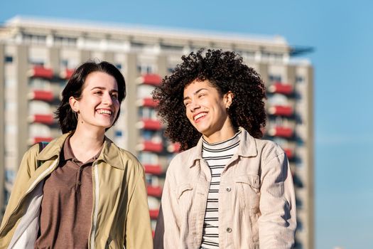 interracial couple of young women walk around the city while smiling funny and happy, concept of female friendship and racial diversity