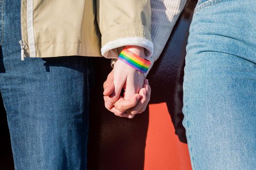detail of the linked hands of two women with a bracelet in the colors of the rainbow flag of the struggle for homosexual rights, concept of sexual freedom and diversity