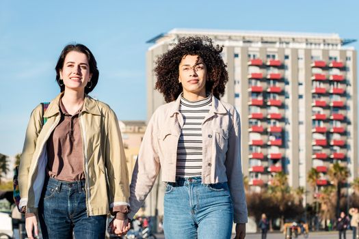 young interracial couple of girls walk around town holding hands, concept of sexual freedom and racial diversity