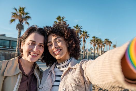 selfie photo of young interracial couple of beautiful girls in a palms and blue sky background, concept of female friendship and racial diversity