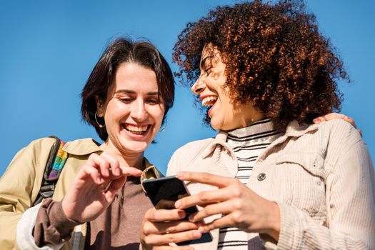 multiracial couple of young women looking at a cell phone while laughing funny, concept of technology and racial diversity