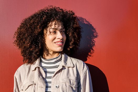 portrait of a beautiful smiling black woman with curly afro hair on a red background, concept of beauty and diversity