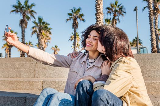 interracial couple of young women doing a self photo with a mobile phone while kissing, concept of female friendship and racial diversity