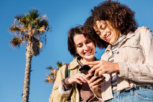 multiracial couple of young women looking at a cell phone while smiling, concept of technology and racial diversity